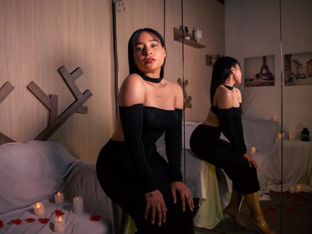 SaharaArisa with dark hair, wearing an off-shoulder black dress, sitting on a stool, reflection in mirror, candles, rose petals, yellow boots, serious expression, bedroom setting.