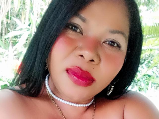 Keilathompson a les cheveux noirs et lisses, du rouge à lèvres rose, du blush rouge, et un collier de perles avec des boucles d'oreilles. Elle regarde l'appareil photo avec un léger sourire, montrant son nez et ses lèvres..
