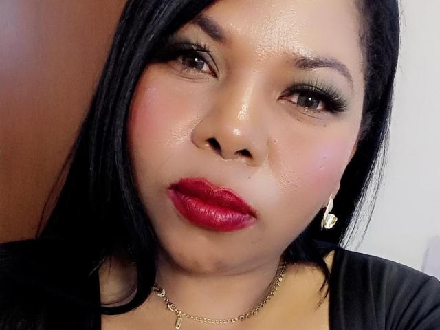 Keilathompson a une peau asiatique brillante et moite, des cheveux noirs, du rouge à lèvres et des boucles d'oreilles dorées. Elle porte un haut noir avec un collier en or. Ses seins ne sont pas visibles..