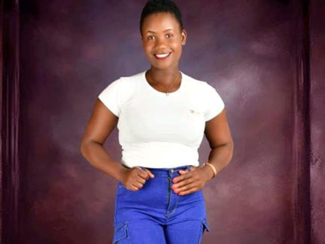 CreamPieQueen stands centered against a purple background. She has dark skin, a bright smile with red lipstick, and her hair is in a tight bun. She wears a white, short-sleeved, slightly form-fitting t-shirt and high-waisted blue jeans with her hands resting on her hips. Her nails are painted red. The image is clear, focusing on her, with no visible text or watermarks.