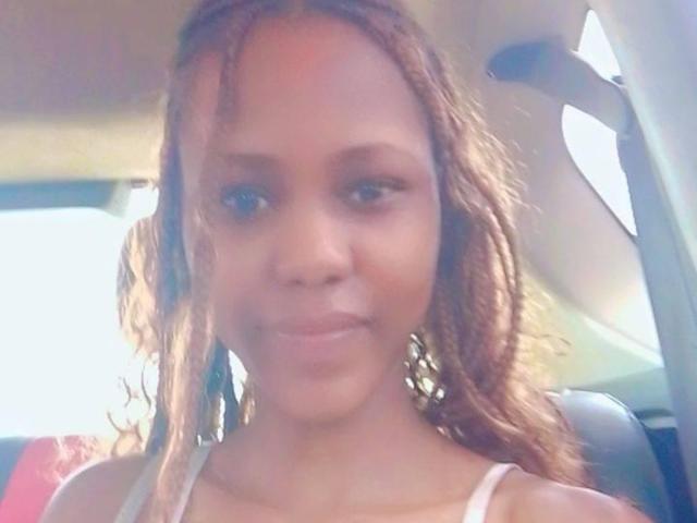 HotyBarbarha has brown, wavy hair, small nose, and a slight smile in a car, wearing a white top, with subtle makeup. Her ass is not visible.