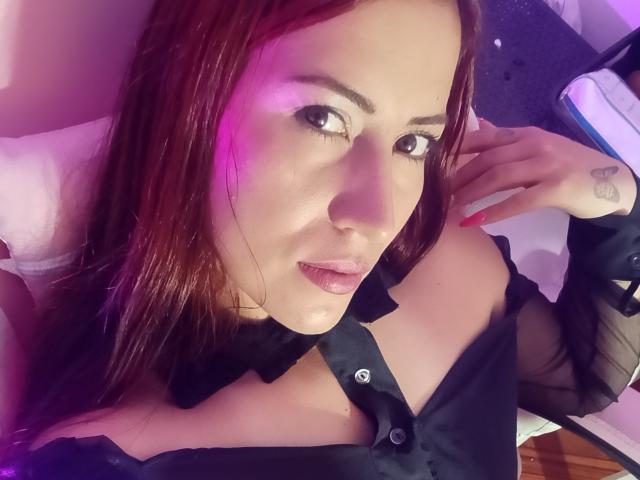 SofiaFountaine with red hair, black button-up shirt, and pink lipstick, showing her tits, pink nails, and a small tattoo on her right hand. Purple light in background.