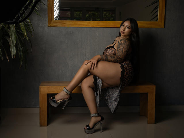 MiaSuarez with tattoos, sitting on a wooden bench, wearing leopard print lingerie, black high heels, legs crossed, showing her ass, long black hair, looking at camera.