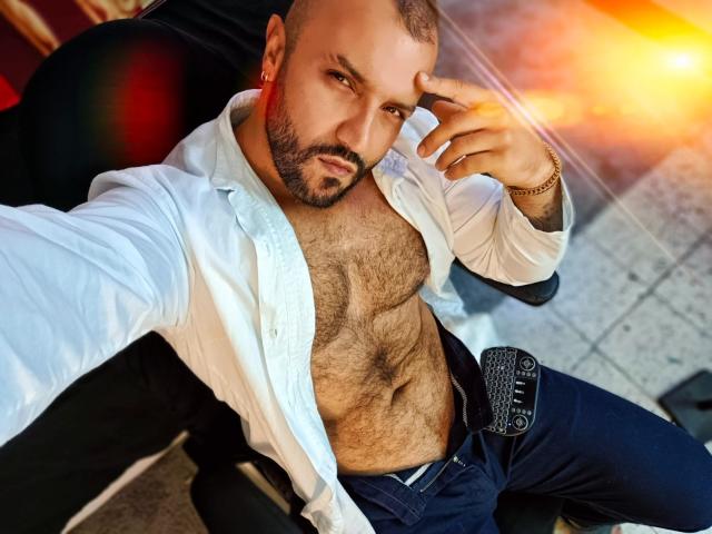 BardoCkroy69, shirtless with white button-up, hairy chest, dark blue pants, belt with buckle, gold bracelet, hand on head, looking at camera, sunlight in background, bald with beard.