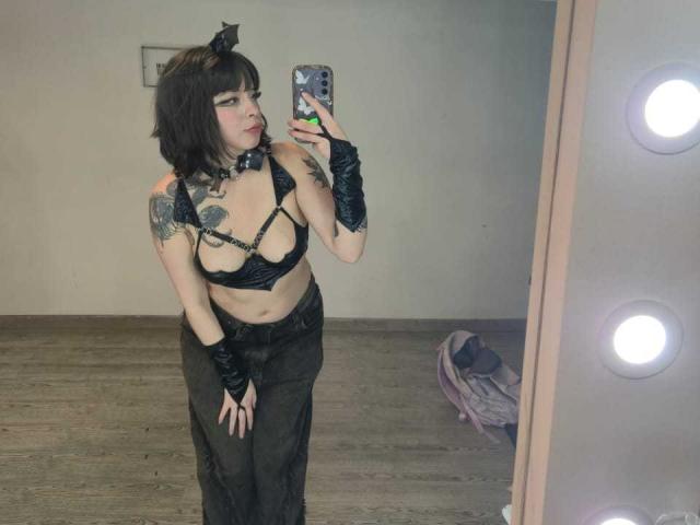 NatashaHottson with black cat ear headpiece, black leather bra showing her tits, black gloves, and dark pants, taking a mirror selfie, showing tattoos on her arm.