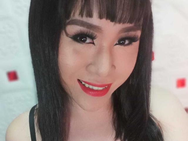 CockZilLaHotTs heeft recht zwart haar, donkere eyeliner, rode lippenstift en ze glimlacht met rood geverfde tanden. Ze draagt een zwarte top met een lichte huidskleur..