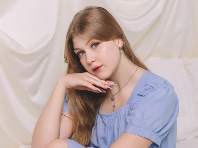 StellaLane with long blonde hair, blue eyes, and pink lips, wearing a blue dress, resting her chin on her hand, showing off her cute ass, and a cross necklace.