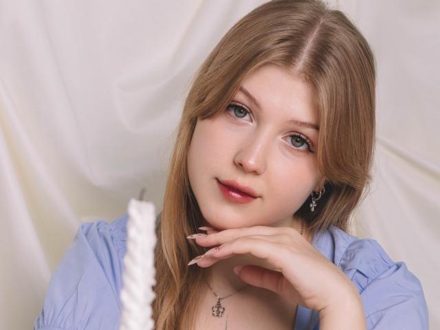 StellaLane with light brown hair, blue eyes, pink lips, wearing a blue shirt, resting her chin on her hand, looking cute and relaxed, showing off her pretty face and tits.