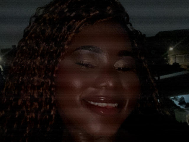 Dilay's dark brown face with closed eyes and smiling, showing white teeth, with braided hair, has a slight film grain texture, looking happy and relaxed.