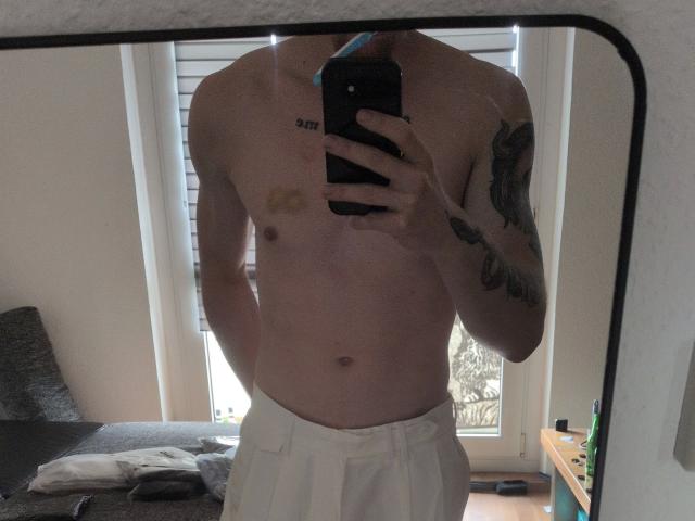 Honig96-hot's shirtless mirror selfie, showing a tattooed arm, bandage on chest, white pants, and a phone covering face. Honig96-hot's flaccid, uncut, and has a slim build.