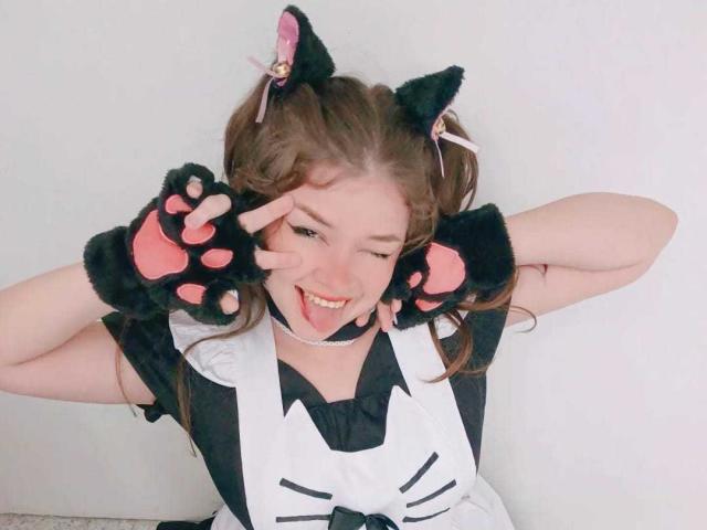 EvaRavissante with cat ears, black paw gloves, and tongue out, wearing a black and white maid outfit, smiling with hands on her ears, looking cute and playful.