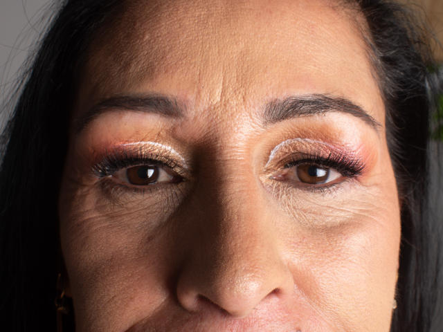 ScarlettSweet's face with brown eyes, dark eyebrows, and tan skin, wearing shiny pink and gold eyeshadow, showing slight wrinkles and black hair on the sides.