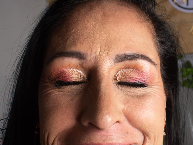ScarlettSweet's face showing wrinkled skin, pinkish-red eyeshadow, and black eyeliner with her eyes closed, black hair, and a slight smile. Her nose and lips are visible.
