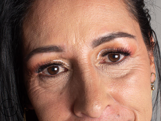 ScarlettSweet's face, showing brown eyes, shiny gold eyeshadow, dark eyebrows, slight smile, black hair, small nose, and a pierced lower lip with a gold stud.