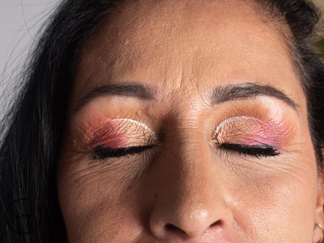 ScarlettSweet's face with her eyes closed, showing off pink and orange shimmer eyeshadow, black eyeliner, and slightly wrinkled skin. She has dark hair and a brown complexion.