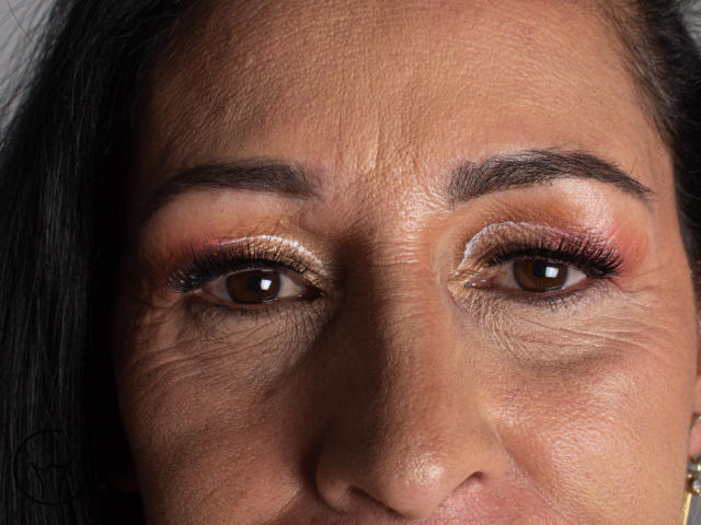 ScarlettSweet's face with brown eyes, shiny copper eyeshadow, and slightly wrinkled skin, showing dark eyebrows and black hair. Her eyes are focused, and her expression is neutral.