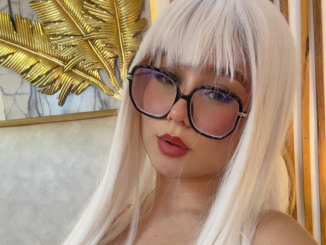 Millie Reed, avec ses cheveux blancs, ses lunettes à monture noire et son rouge à lèvres rouge, exhibant ses lèvres pulpeuses et aguicheuses, a l'air incroyablement sexy..