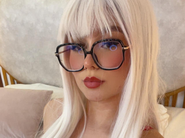 MillieReed with blonde hair, black glasses, and red lipstick, showing off her pouty ass-kissing face, looking straight at the camera.