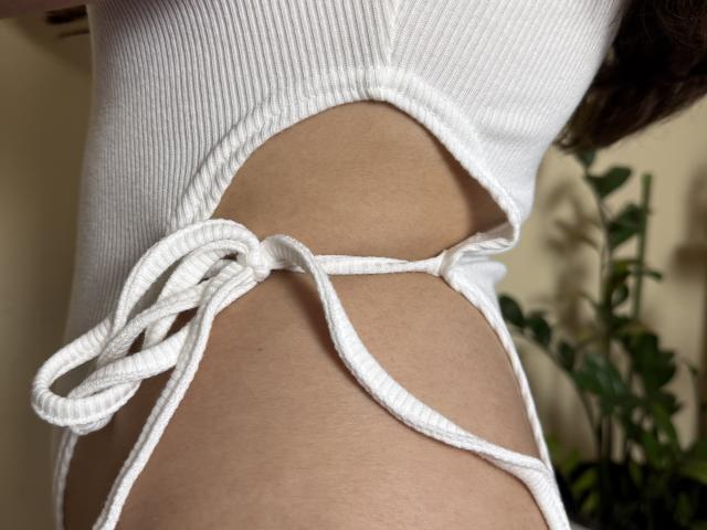 Symphoniia's white ribbed bikini bottom with side ties, exposing her smooth tan skin and small, curvy ass. The fabric is tight, highlighting her slim, sexy figure.