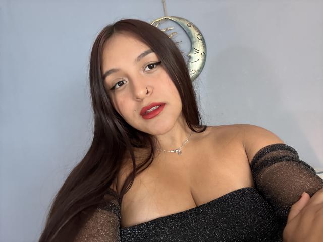 MarianaVargasX with long brown hair, red lipstick, nose ring, off-shoulder black sparkly top, visible boobs, light skin, subtle makeup, silver necklace, looking at camera.