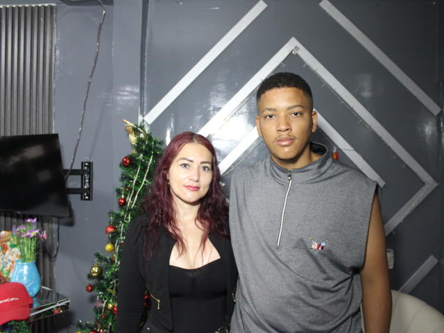 ErosAndEva with red hair, black top, and tits, stands next to Eva with short black hair, gray sleeveless shirt, and a small dick pocket, in a room with a Christmas tree.