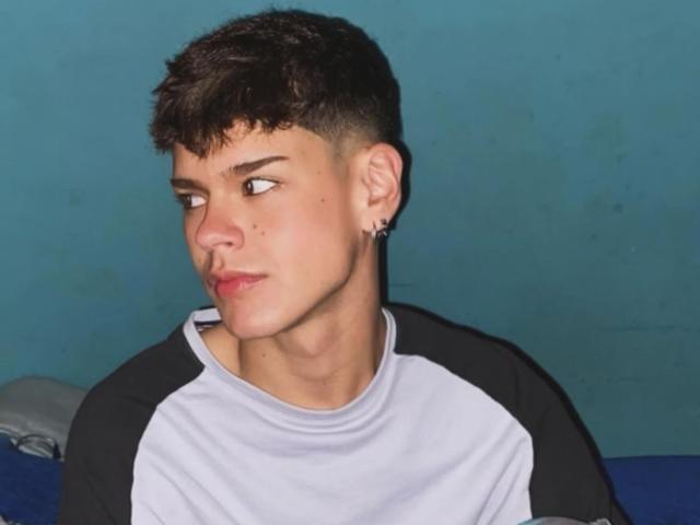 KevinMiet has short, curly brown hair, a black and white raglan shirt, and a small ear piercing. He's looking to the side with a slightly pouty expression.