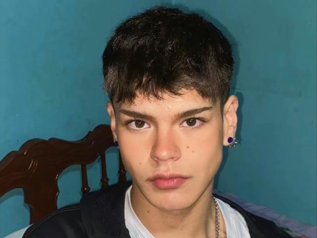 KevinMiet has short black hair, dark eyebrows, and a serious face with a nose piercing and black ear studs. He wears a black jacket over a white shirt.