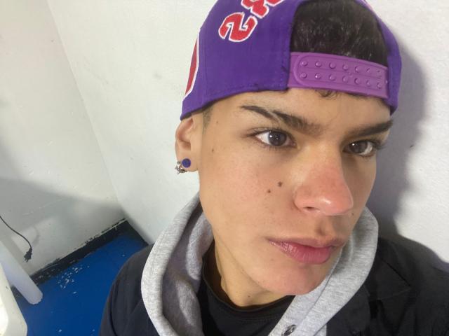 KevinMiet has a purple backwards cap, small nose, pierced ear, black shirt, gray hoodie, and a slight pout, with brown eyes and a light skin tone.