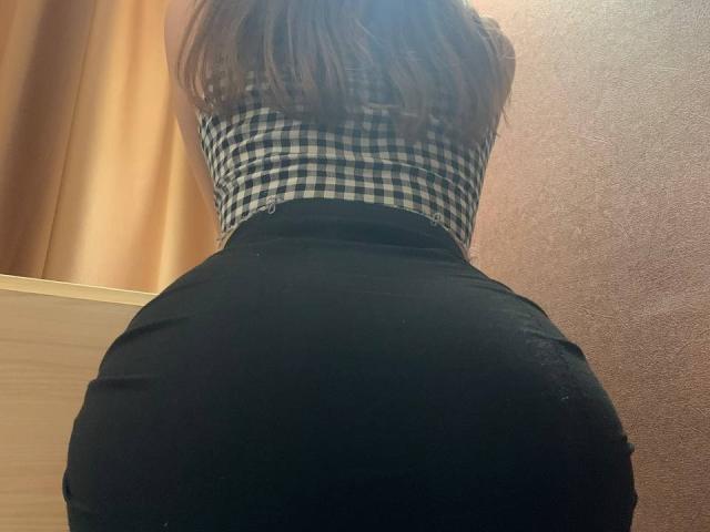 MoonLiza's butt is in a tight black skirt, wearing a black-and-white checkered top, standing with her back to the camera, showing her curvy, round butt.