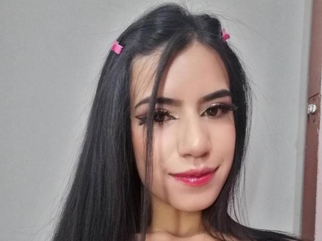 SamiLure, avec ses longs cheveux noirs tressés en couettes, ses pinces à cheveux roses, son eye-liner épais et ses lèvres roses brillantes, sourit à l'appareil photo. Elle a un look mignon et séduisant..