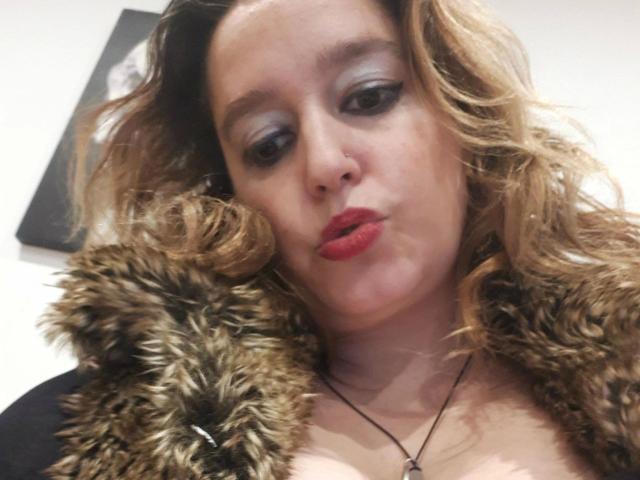Anita: De piel morena, con un abrigo de pelo marrón, lápiz labial rojo, cabello rubio rizado y maquillaje de ojos ahumado, haciendo una mueca. Los senos ligeramente visibles. Collar con un pequeño colgante..