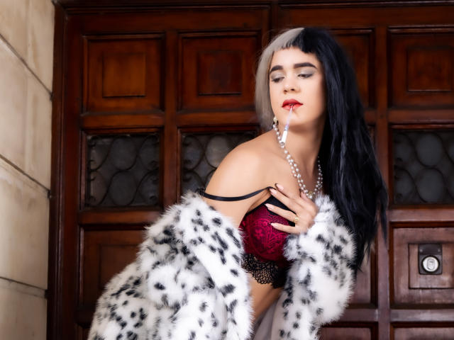 AliceCoolenk with black-and-white hair, wearing a red lace bra, pearl necklace, and a white fur coat, has a pearl earring in her mouth, showing her tits.