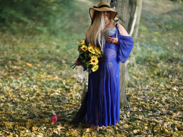 Hotferkel-sex with long blonde hair, wearing a blue dress, sun hat, holding sunflowers and blue fabric, standing by a tree, with a red flower on the ground.