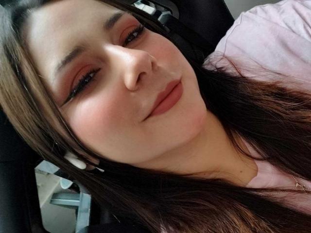 CandyI a la peau brun clair, de longs cheveux bruns, et un maquillage rose, avec un léger sourire qui révèle ses lèvres roses. Elle porte une chemise rose et a un casque sur la tête..