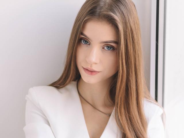 EricaDiaz has long, straight brown hair, blue eyes, and a slight smile, wearing a white shirt, with a delicate necklace, looking cute and sexy.