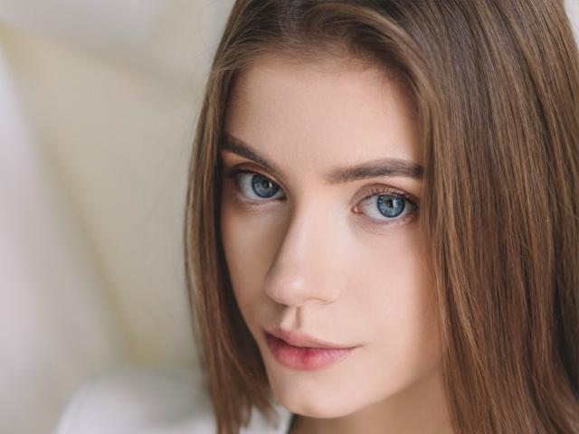 Erica Diaz tiene ojos azules, cabello lacio de color castaño claro, y un rostro liso de piel clara con labios rosados, mirando directamente a la cámara con una sonrisa leve y segura..