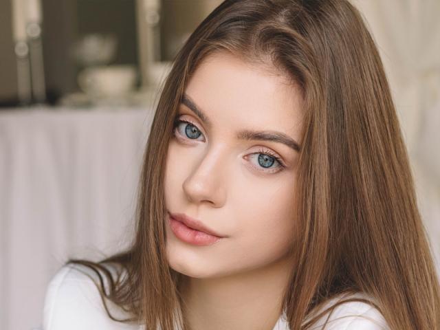 EricaDiaz has blue eyes, light brown straight hair, and a cute face with pink lips. She's wearing a white top, and her smooth skin is slightly flushed.
