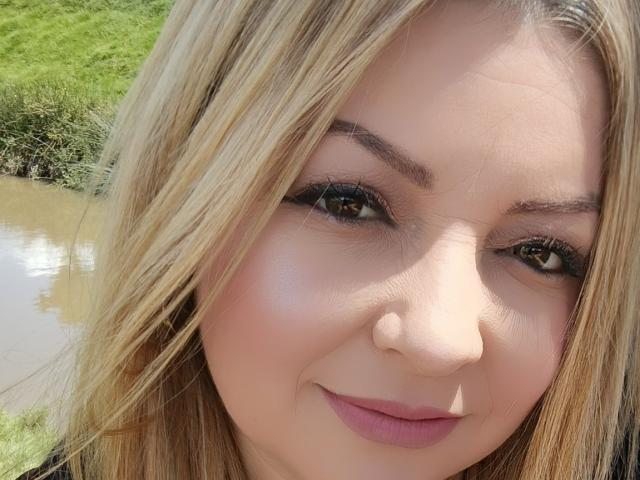 NatalyHami's face with blonde hair, green eyes, black eyeliner, pink lipstick, and a slight smile, showing a cute, sexy, and attractive look. Her nose is cute too.