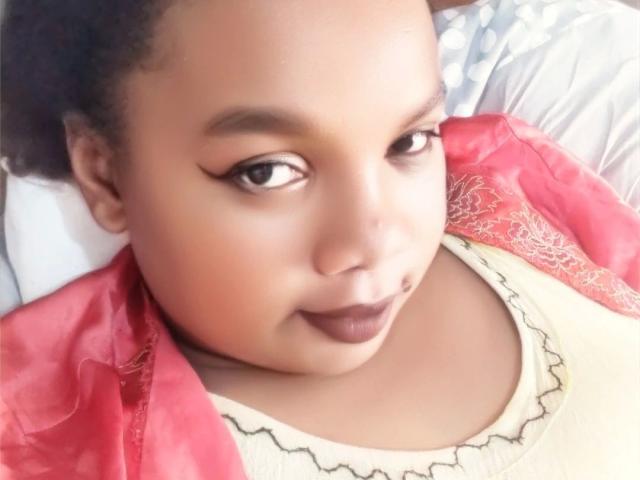 Leylahwilliam-hot with light brown skin, dark lipstick, and eyeliner, wearing a red lace shirt over a cream top, looking up with a slight smile.