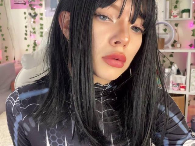 AmeliaAley with black hair, red lipstick, and blue eyes, wearing a black Spider-Man suit, has a cute face, medium tits, and a sexy look, in a bedroom.
