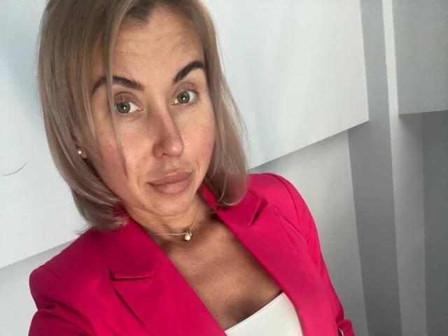 StephieRose has light brown hair, green eyes, and a pink blazer over a white top, wearing a pearl necklace with small earrings. She's smiling subtly.