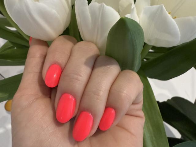 Elionoria's hand with bright neon pink nails, holding white tulips. Her skin is light, and the green tulip leaves are visible. She's gripping the flowers gently.
