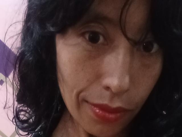 KarolineS has curly black hair, brown eyes, and red lips with a subtle smile. Her slightly wrinkled skin is visible, and she's wearing a black top.