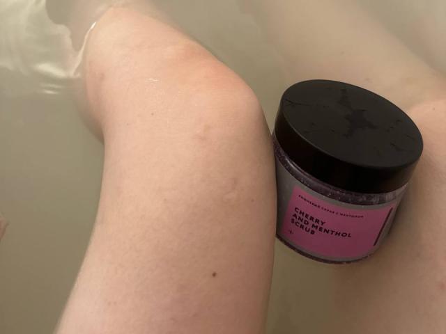 Michelleandjames's knee is in the water with a black-capped jar of Cherry Coconut Scrub. The jar is on Michelleandjames's thigh.