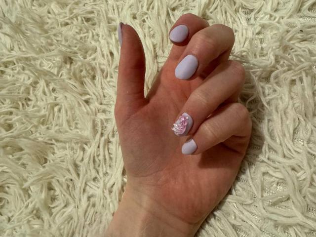 Michelleandjames's hand with pale purple nail polish and a pink floral design on the ring finger, resting on a fluffy white rug.