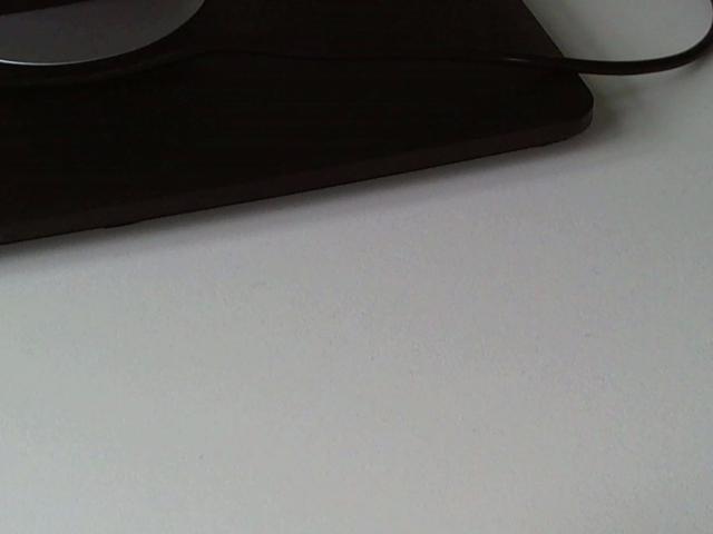 Black mouse pad with a black cord and a partial white desk in the background. The cord is slightly visible, extending from the top right.