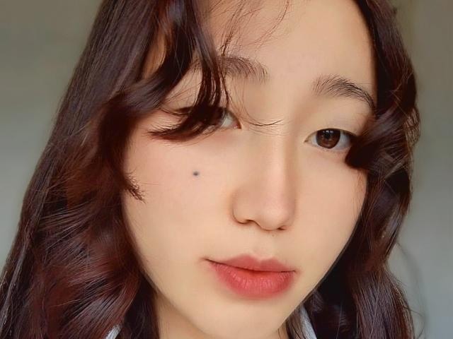 AmorBae a les cheveux bruns ondulés, un œil fermé, une petite tache noire sur sa joue gauche et des lèvres rosâtres. C'est une femme asiatique mignonne avec une expression neutre..