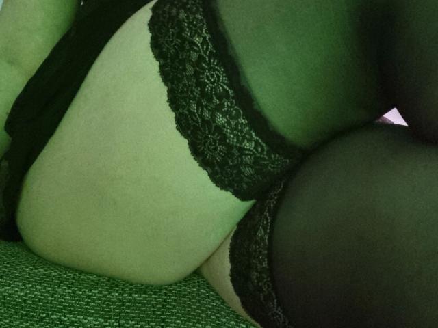 Curvy-selin-hot's ass in black lace lingerie and sheer stockings, lying on a green textured surface. The green lighting enhances the sensual, intimate vibe.