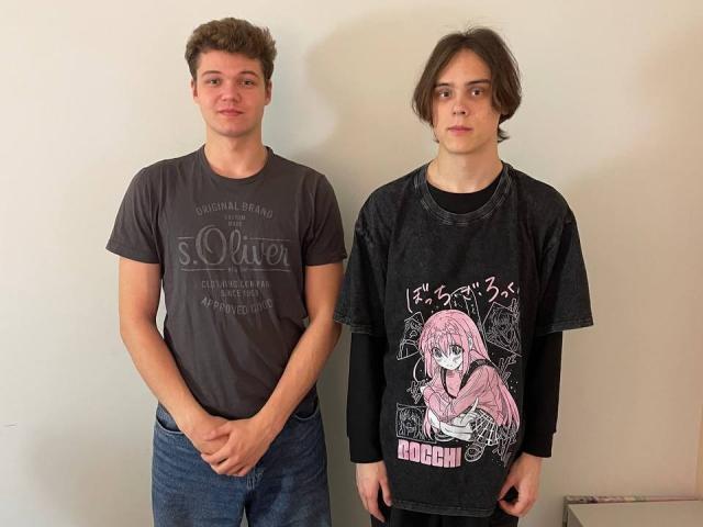 LucasKarl with curly brown hair, gray shirt, blue jeans, standing next to LucasKarl with shaggy brown hair, black graphic shirt, black long sleeves, both looking serious.