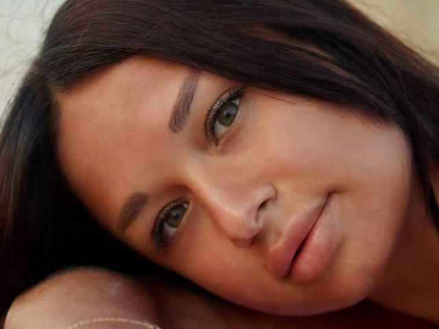 MaryLoveX's face with brown eyes, dark eyebrows, and a slight smile, looking relaxed. She has long brown hair and a smooth, tan skin tone. Her lips are gently parted.